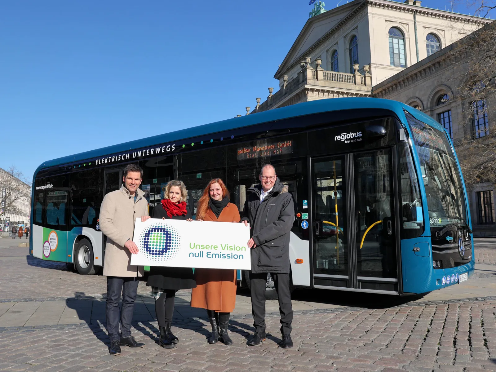 Ein Elektrobus auf dem Opernplatz in Hannover. Im Vordergrund stehen Regionspräsident Steffen Krach, Regiobus-Geschäftsführerin Elke Maria van Zadel, Regiobus-Geschäftsführerin Denise Hain und Verkehrsdezernent Ulf-Birger Franz.